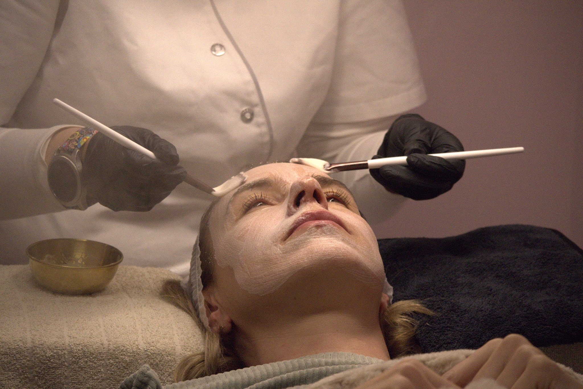 Gezichtsbehandeling in de salon: een masker wordt met twee kwasten aangebracht